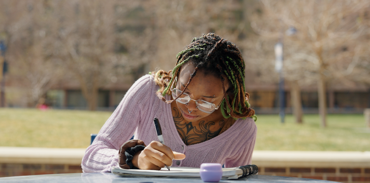 Ann-Adele Blassingame sitting on a table outside drawing