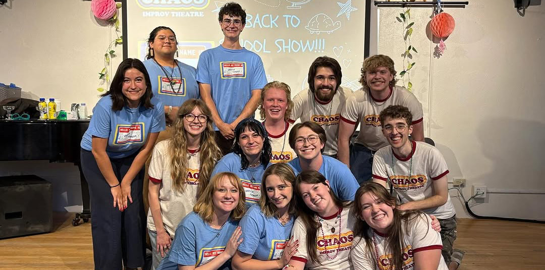 A group of students some standing and some sitting on a stage smiling