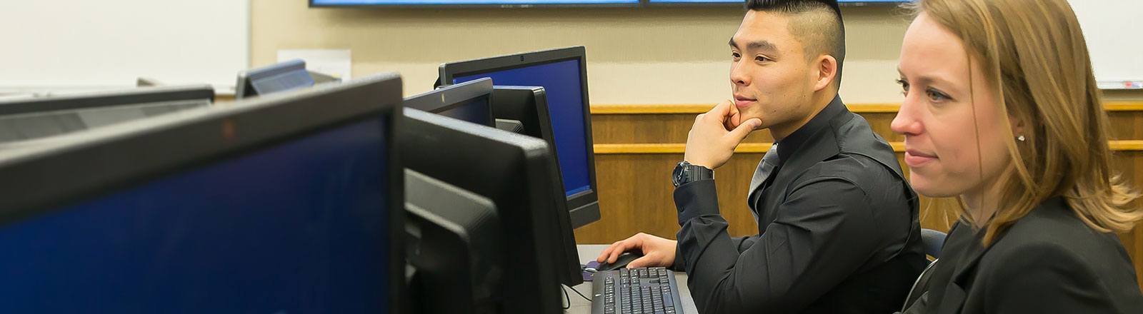 Two business students sitting at desk looking at computer screen