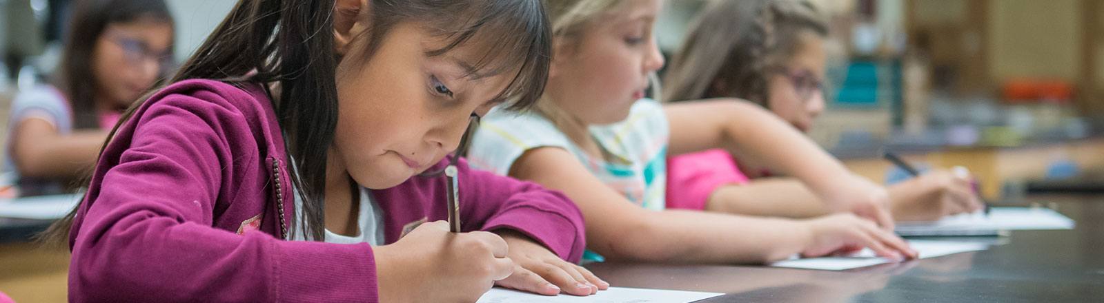 Group of students sitting at table drawing in art class