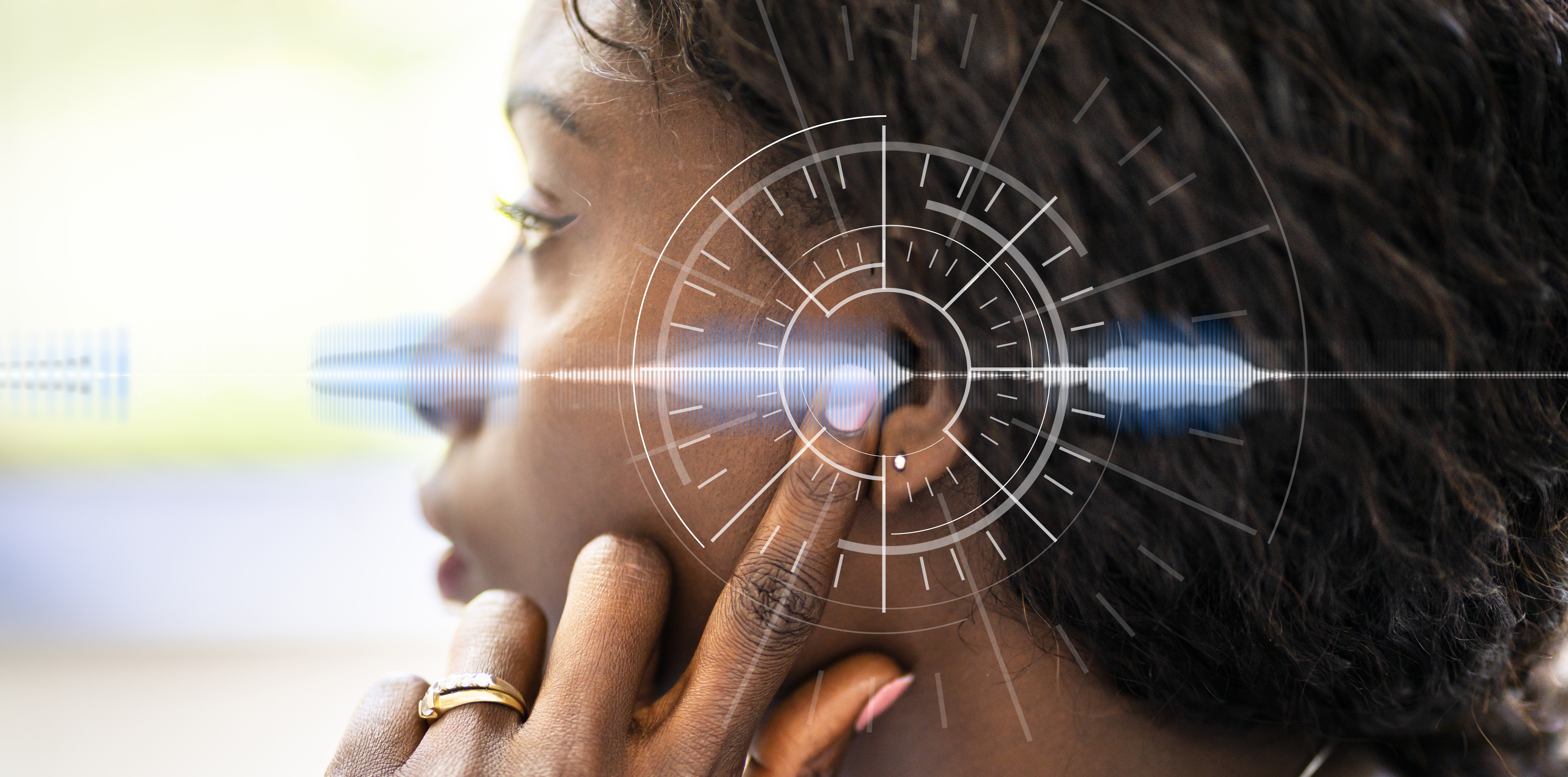 Side profile of a woman wearing a hearing aid with her finger to her ear.