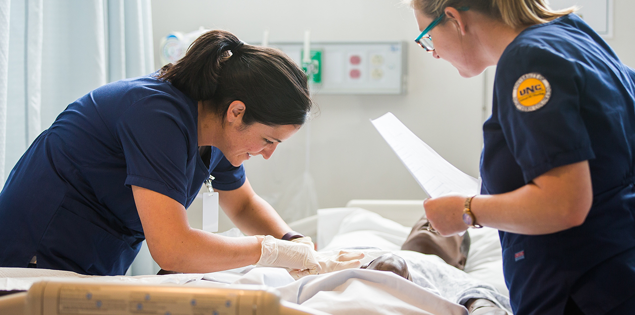 two female nursing students attending to a manikin patient in a bed