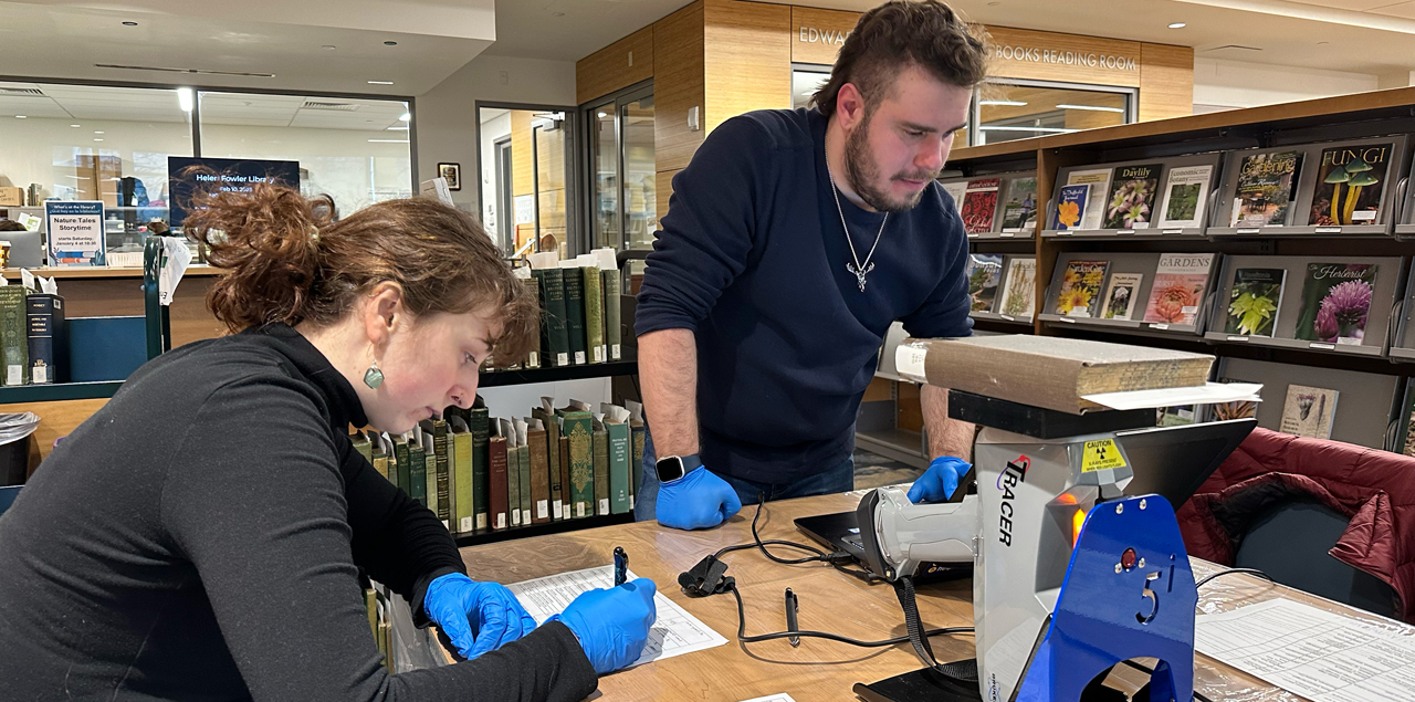 Two students sitting at a table in a library using the xrf spectrometer on rare books.