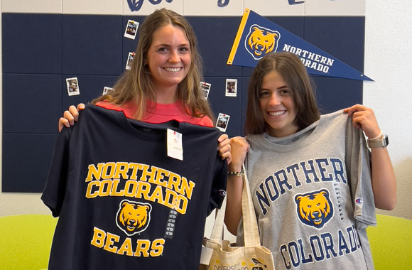 Two students holding t-shirts in the Graduate School office.