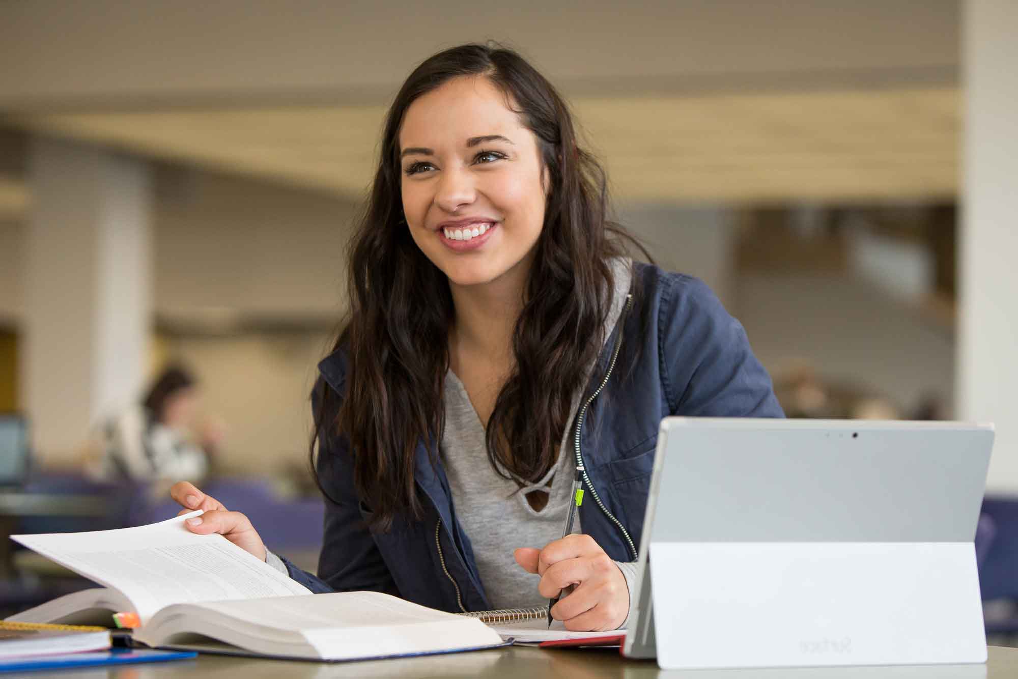 Transfer student sitting at work desk on UNC campus with a book an ipad.