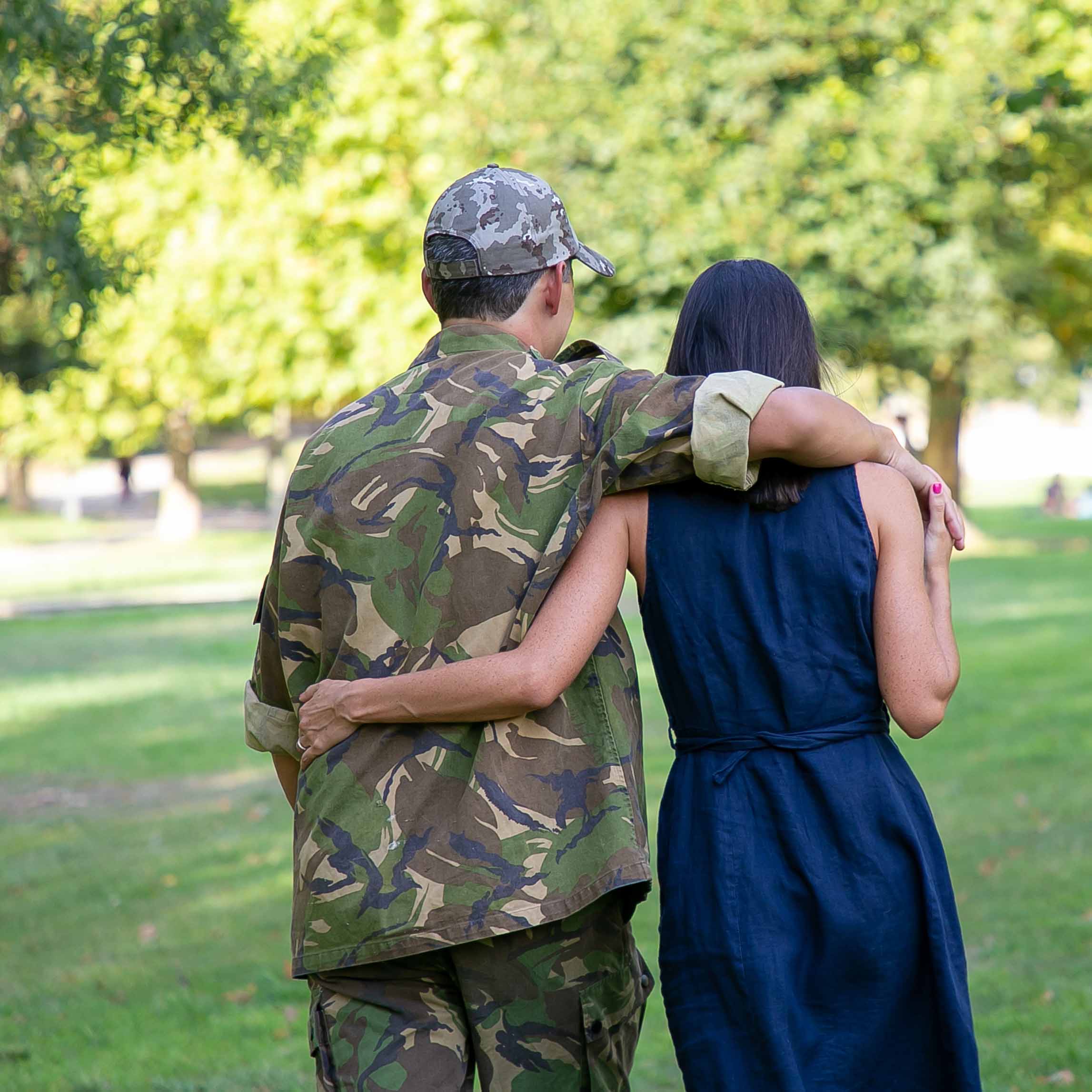 A man in the military walking with his arm around a woman.