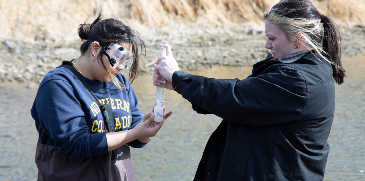 Two students conducting water monitoring work in the Poudre River.